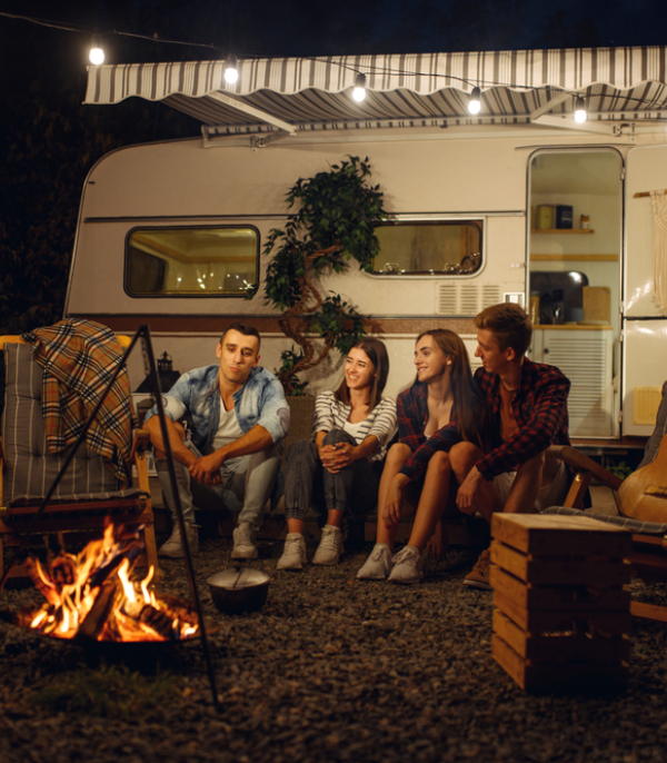 Friends sitting by a campfire at night during camping at a caravan